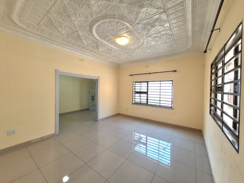 Spacious living area featuring classic ornate pressed metal ceilings, neutral tiled flooring, and security bars on windows, offering a bright and versatile blank canvas.