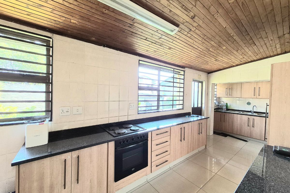 Spacious kitchen featuring light wood cabinetry, granite countertops, built-in oven and hob, and a distinctive timber-clad ceiling.
