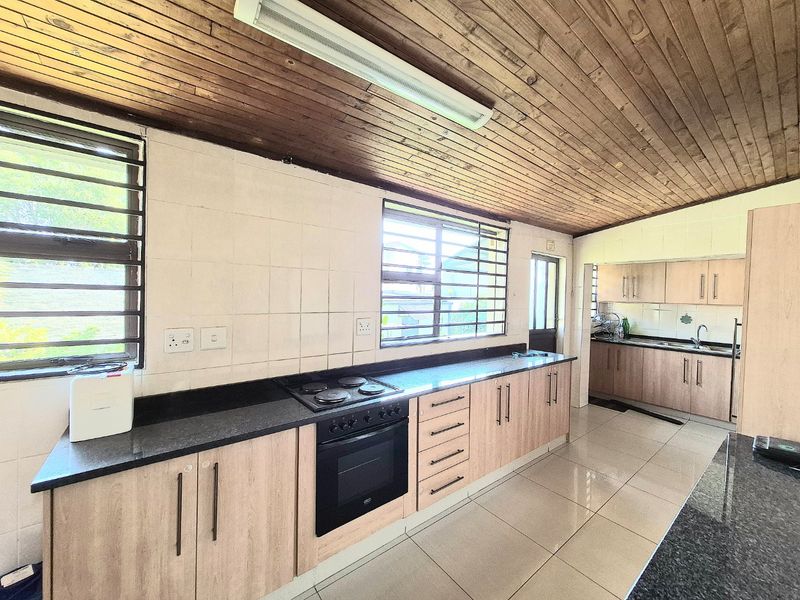 Spacious kitchen featuring light wood cabinetry, granite countertops, built-in oven and hob, and a distinctive timber-clad ceiling.