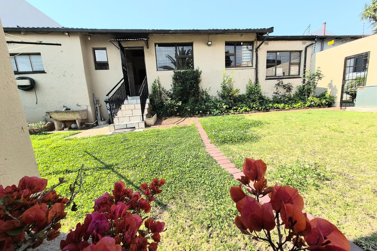 Rear exterior view of the house featuring a small lawn, paved walkway, tiled entrance steps, and security features on windows.