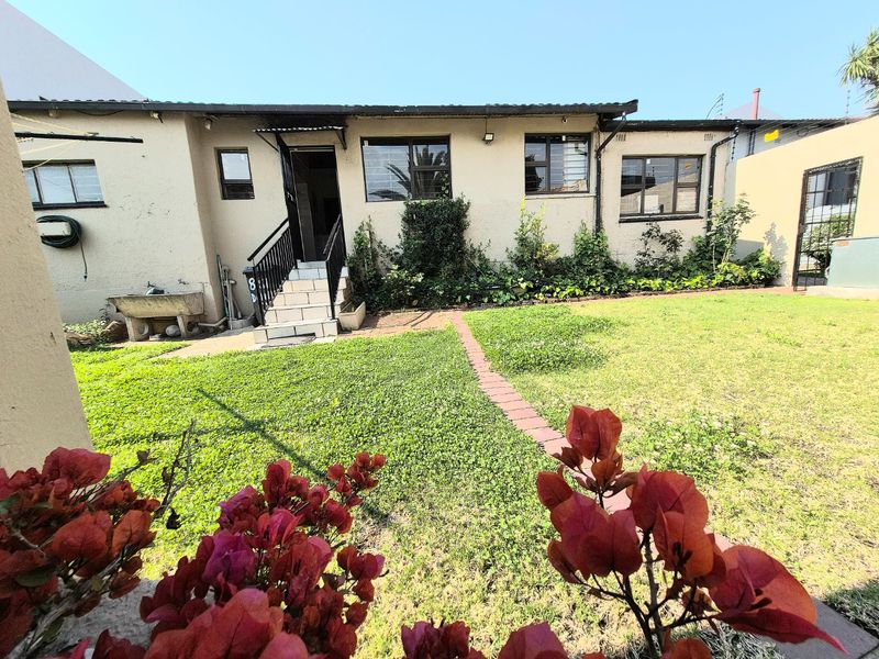 Rear exterior view of the house featuring a small lawn, paved walkway, tiled entrance steps, and security features on windows.