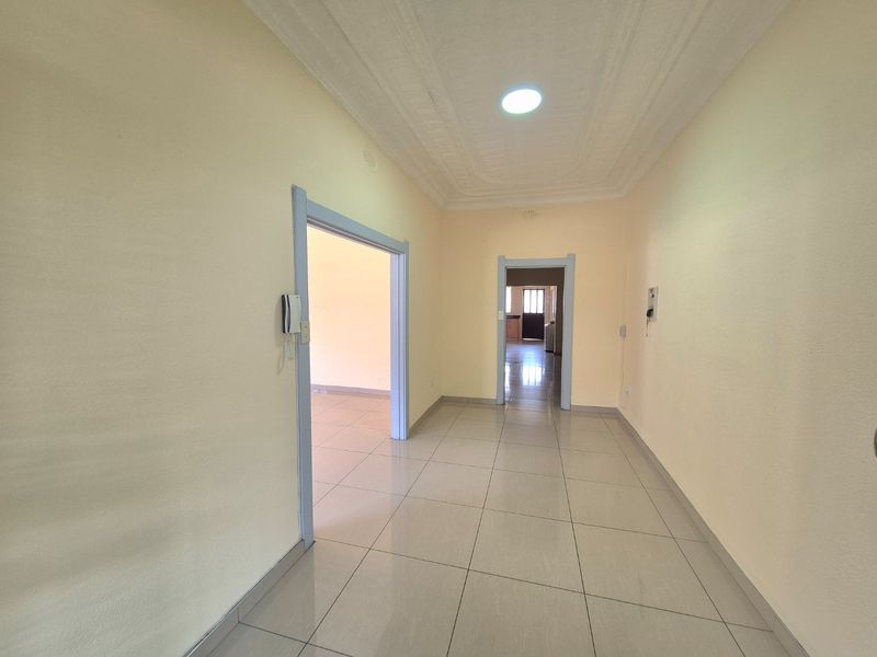 A spacious, empty hallway featuring tiled flooring and a decorative recessed ceiling, providing access to multiple rooms within the home.