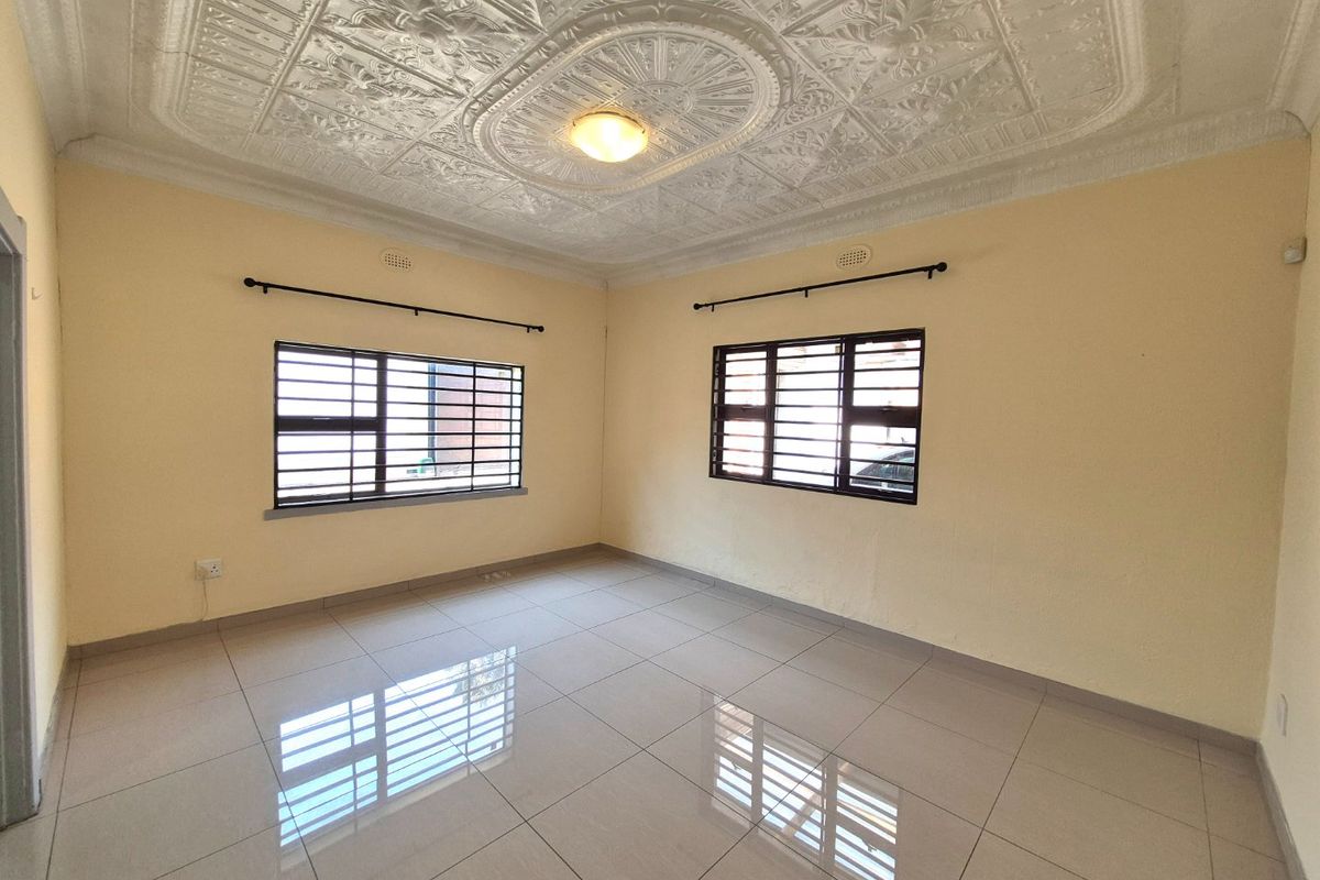 A bright, empty living room featuring polished ceramic floor tiles and a decorative pressed metal ceiling with security-barred windows.