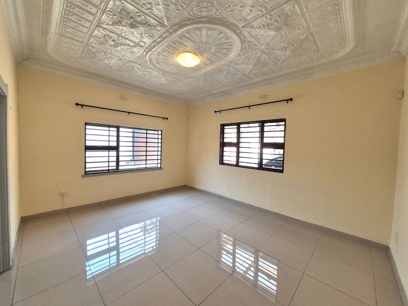 A bright, empty living room featuring polished ceramic floor tiles and a decorative pressed metal ceiling with security-barred windows.