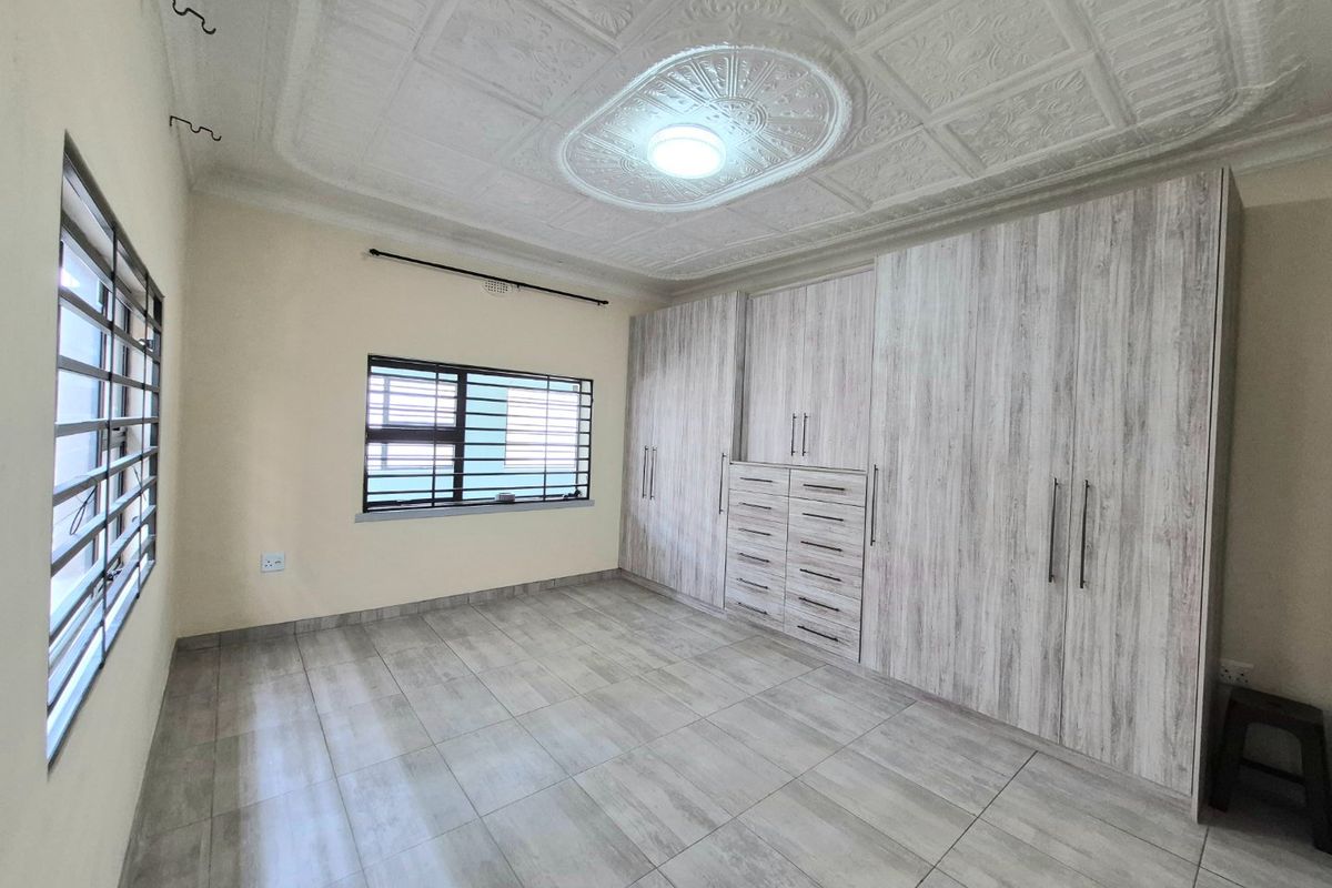 Spacious bedroom featuring modern built-in cupboards, tiled flooring, and an ornate ceiling with a central light fixture.