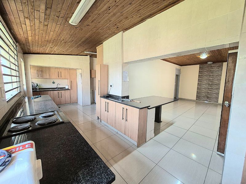 Spacious open-plan kitchen and living area featuring granite countertops, built-in cabinetry, electric hob, and tiled flooring with a timber-clad ceiling.