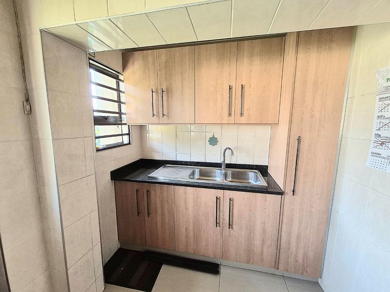 A functional kitchen featuring light wood-tone cabinetry, granite countertops, a double stainless steel sink, and tiled finishes throughout.