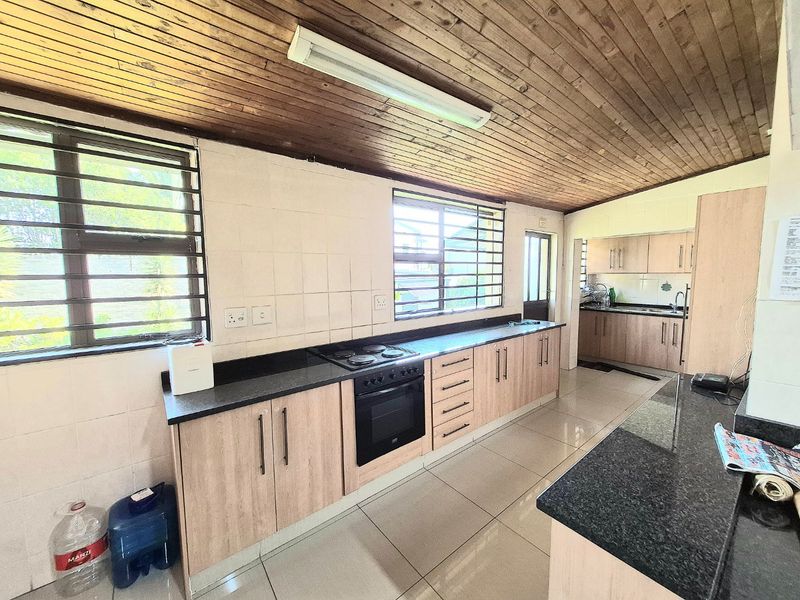 Spacious kitchen featuring granite countertops, built-in oven and hob, ample cabinetry, and a distinctive timber ceiling with tiled flooring throughout.