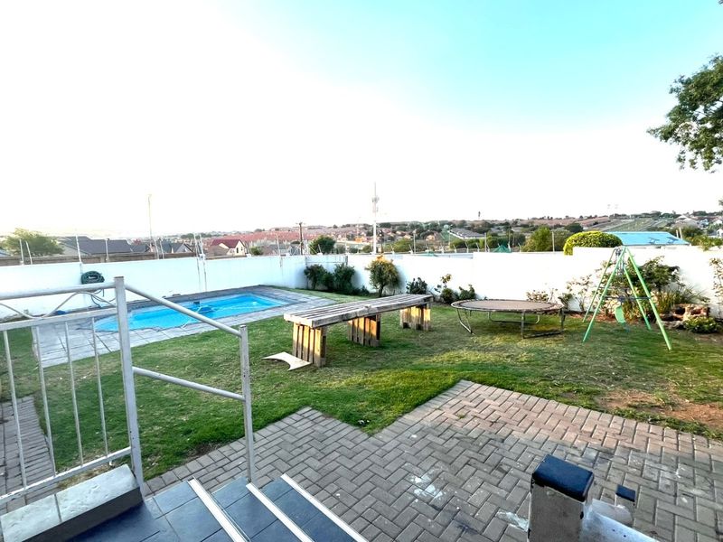 Rear garden area featuring a swimming pool, paved patio space, and perimeter wall with security fencing, offering an elevated view of the surrounding neighborhood.