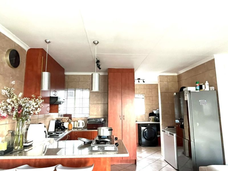 Open-plan kitchen featuring wood-finish cabinetry, granite countertops, gas hob, and integrated laundry area with tiled finishes throughout.