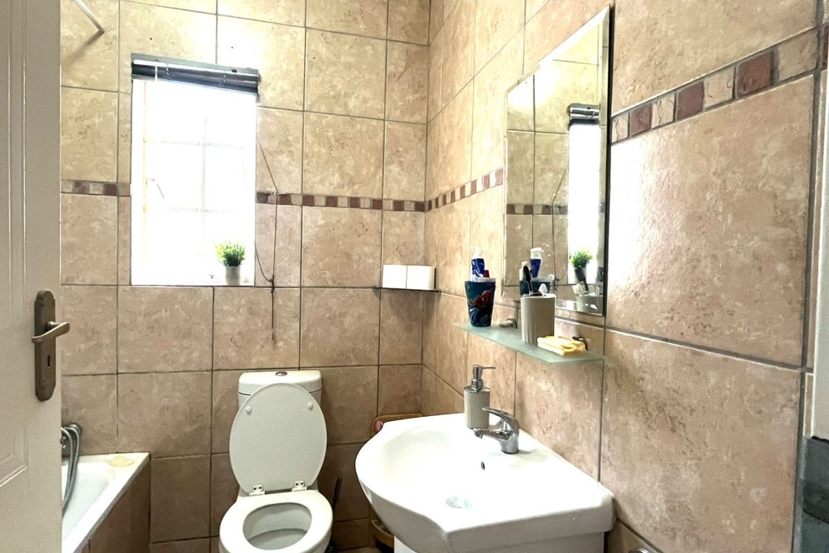 A functional bathroom featuring full-height ceramic wall tiling, a pedestal washbasin, a toilet, and a bathtub with a window for natural light.