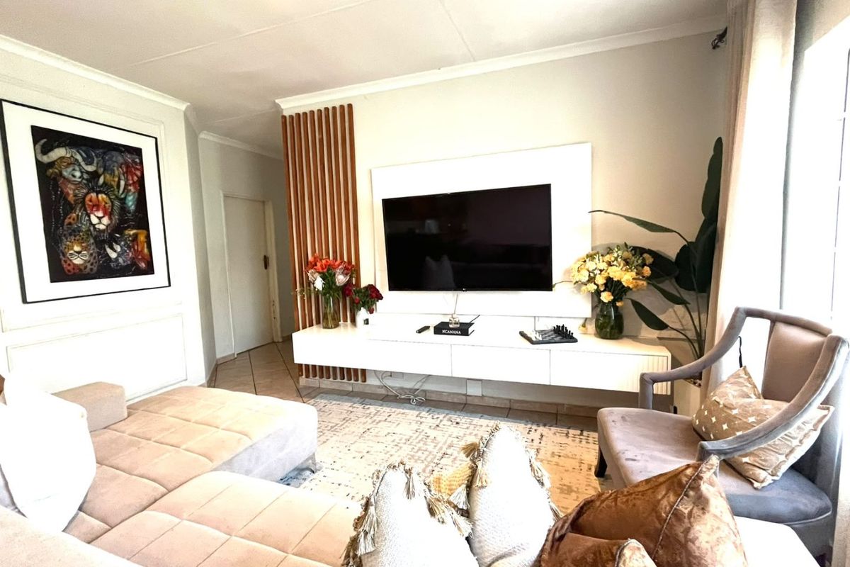 A well-maintained living room featuring a modern wall-mounted media console, decorative timber slat paneling, and neutral tiled flooring.