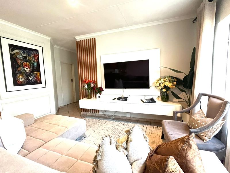 A well-maintained living room featuring a modern wall-mounted media console, decorative timber slat paneling, and neutral tiled flooring.