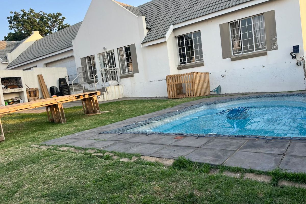 Rear exterior view of the townhouse featuring a swimming pool with safety net, a built-in braai area, and a private garden space.