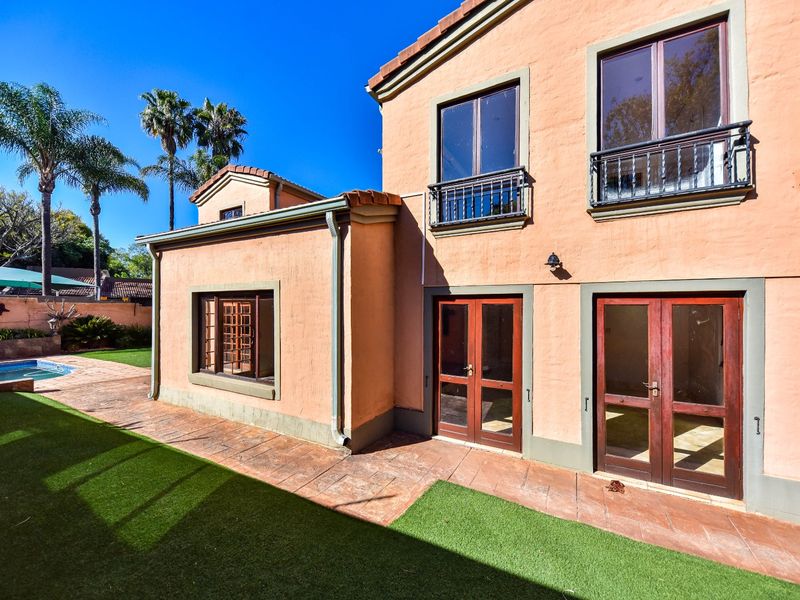 Rear view of the house featuring a stucco facade, timber-framed doors and windows, a paved patio area, and a swimming pool in the garden.