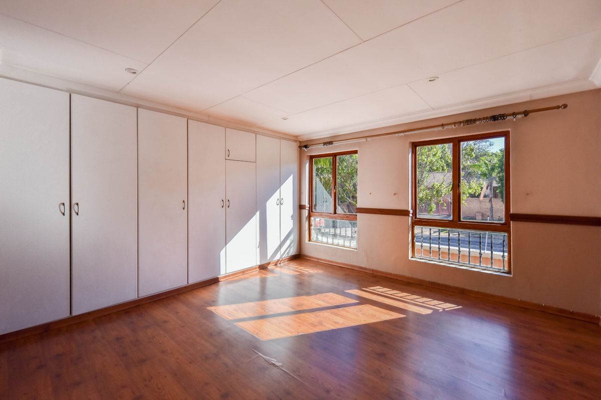 A spacious, empty bedroom featuring extensive built-in cupboards, warm laminate flooring, and large windows that provide ample natural light.