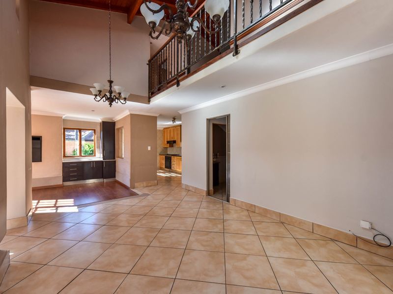 Spacious open-plan living area featuring high ceilings with exposed timber beams, a mezzanine balcony, tiled flooring, and a view into the adjoining kitchen.