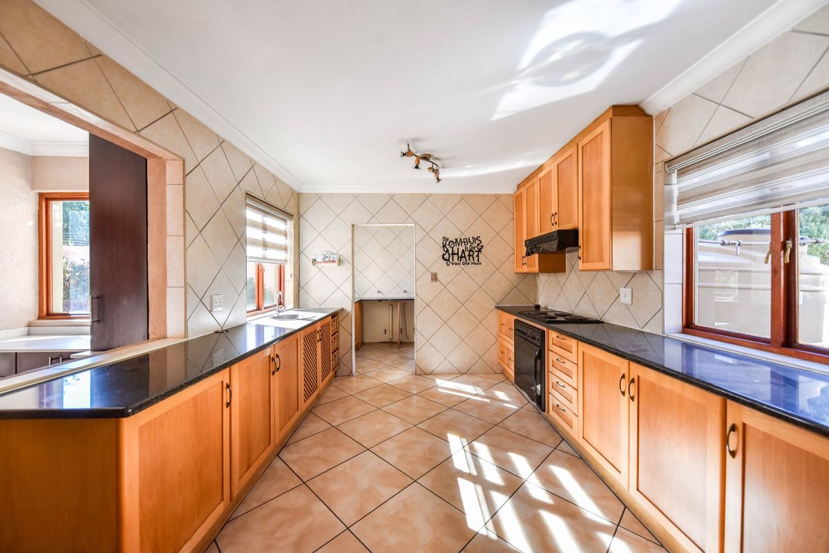 Spacious kitchen featuring wooden cabinetry, granite countertops, integrated oven and hob, and tiled finishes throughout.
