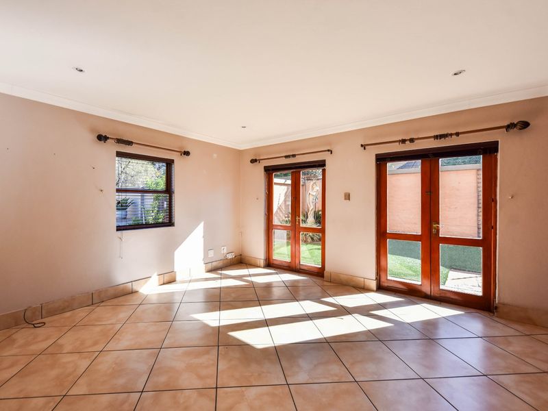Spacious living area featuring neutral tiled flooring, recessed lighting, and multiple wooden-framed glass doors providing direct access to the rear garden.