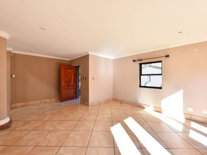 A spacious, empty living area featuring neutral-toned walls, tiled flooring, recessed lighting, and a solid timber entrance door.