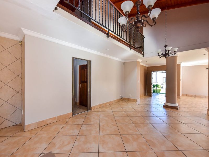 Spacious open-plan living area featuring high ceilings, a mezzanine level with wrought iron balustrade, tiled flooring, and a prominent structural column.
