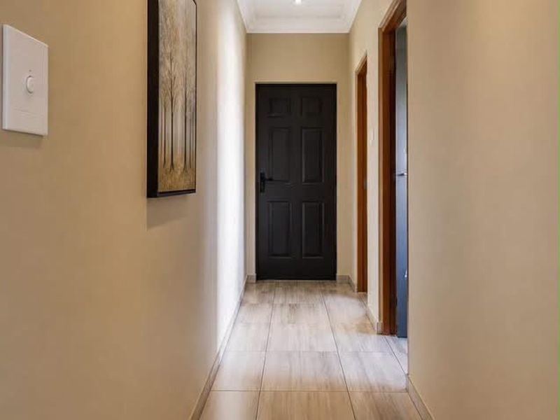 A clean, well-lit hallway featuring neutral wall tones, modern tiled flooring, and a panelled ceiling with recessed lighting.