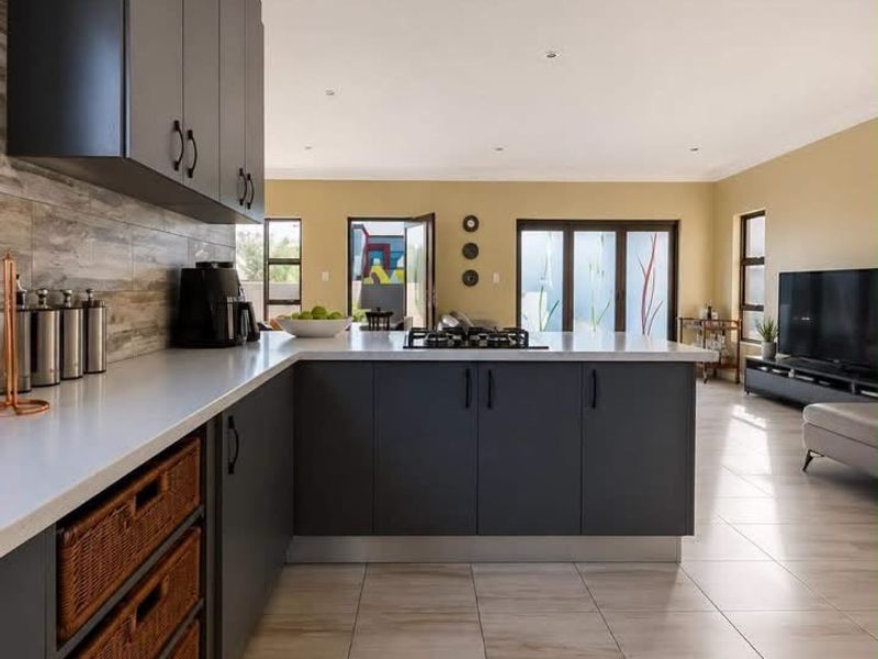 Modern open-plan kitchen and living area featuring sleek dark cabinetry, stone countertops, gas cooktop, and large sliding doors leading to the outdoor space.