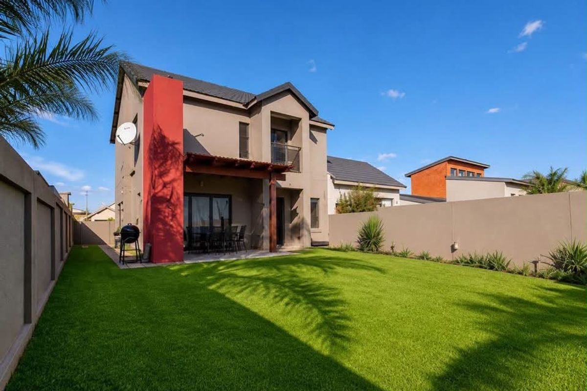 Rear view of a modern two-story house featuring a covered patio with a timber pergola, a well-maintained lawn, and high boundary walls.