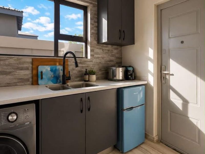 A modern, well-appointed laundry area featuring sleek dark cabinetry, stone countertops, a stainless steel sink, and contemporary tiled finishes.