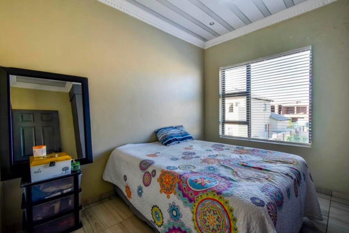 A functional bedroom featuring tiled flooring, a panelled ceiling with decorative cornice, and a window fitted with venetian blinds.