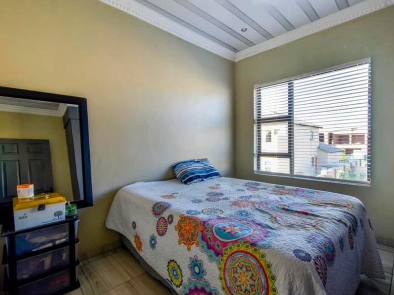 A functional bedroom featuring tiled flooring, a panelled ceiling with decorative cornice, and a window fitted with venetian blinds.