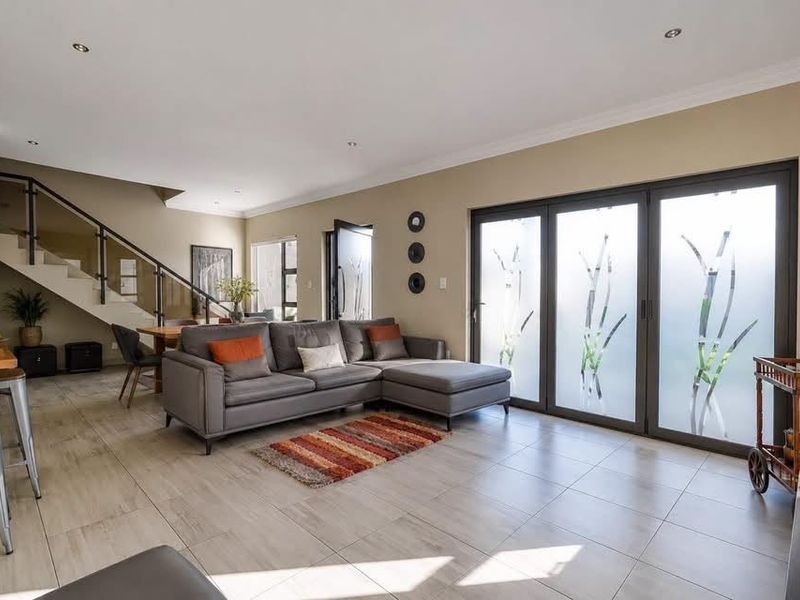 Spacious open-plan living area featuring tiled floors, a modern staircase with glass balustrades, and large bi-fold doors leading to the exterior.