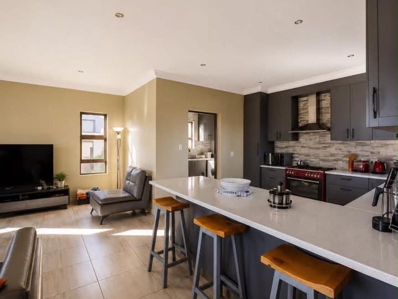 Modern open-plan living area featuring a contemporary kitchen with stone countertops, dark cabinetry, and tiled flooring, seamlessly flowing into the adjacent living space.
