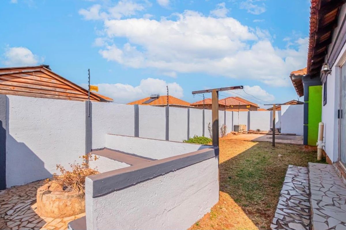 A rear exterior area featuring a perimeter wall with electric fencing, a paved walkway, and a built-in masonry bench in the garden.