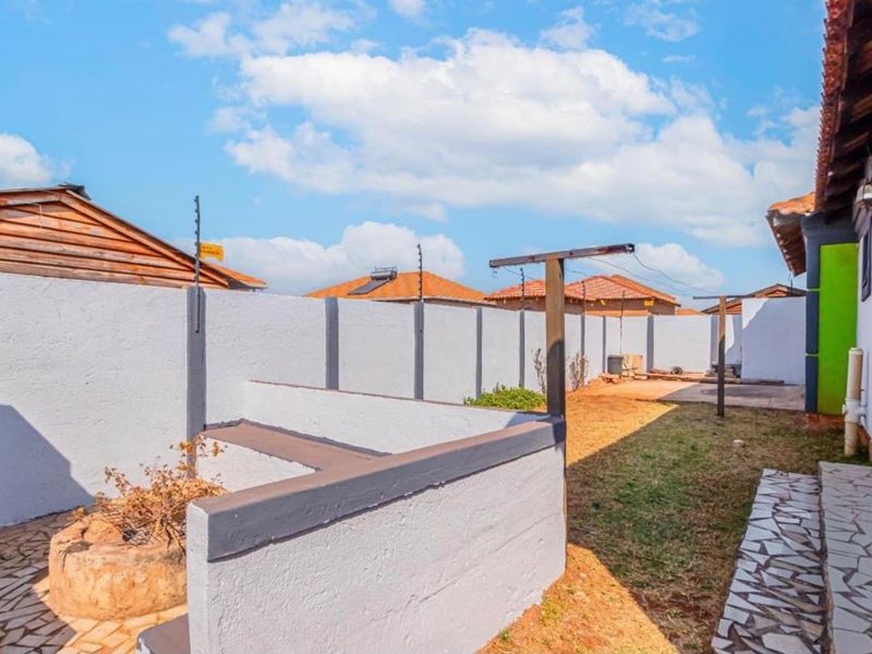 A rear exterior area featuring a perimeter wall with electric fencing, a paved walkway, and a built-in masonry bench in the garden.