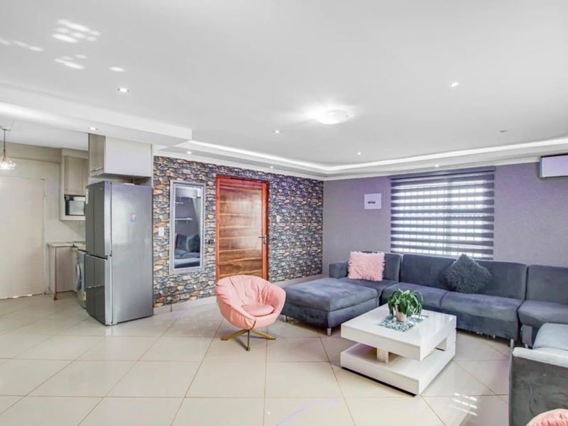 An open-plan living area featuring tiled floors, recessed lighting, a stone veneer feature wall, and an integrated kitchen space with modern finishes.
