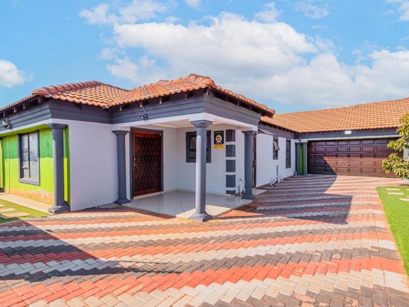 A well-maintained single-story house featuring a paved driveway, covered entrance porch with columns, and an attached double garage.