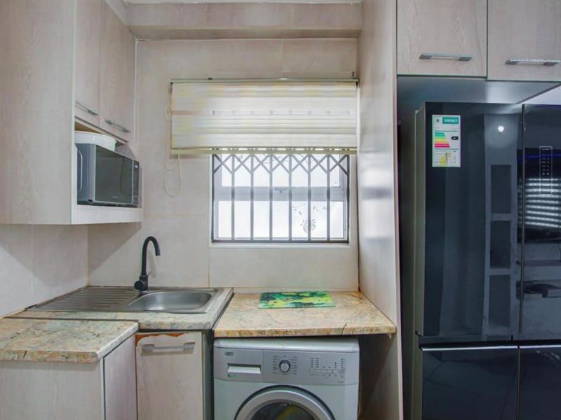 Compact scullery area featuring stone countertops, stainless steel sink, built-in cabinetry, and dedicated space for laundry appliances.