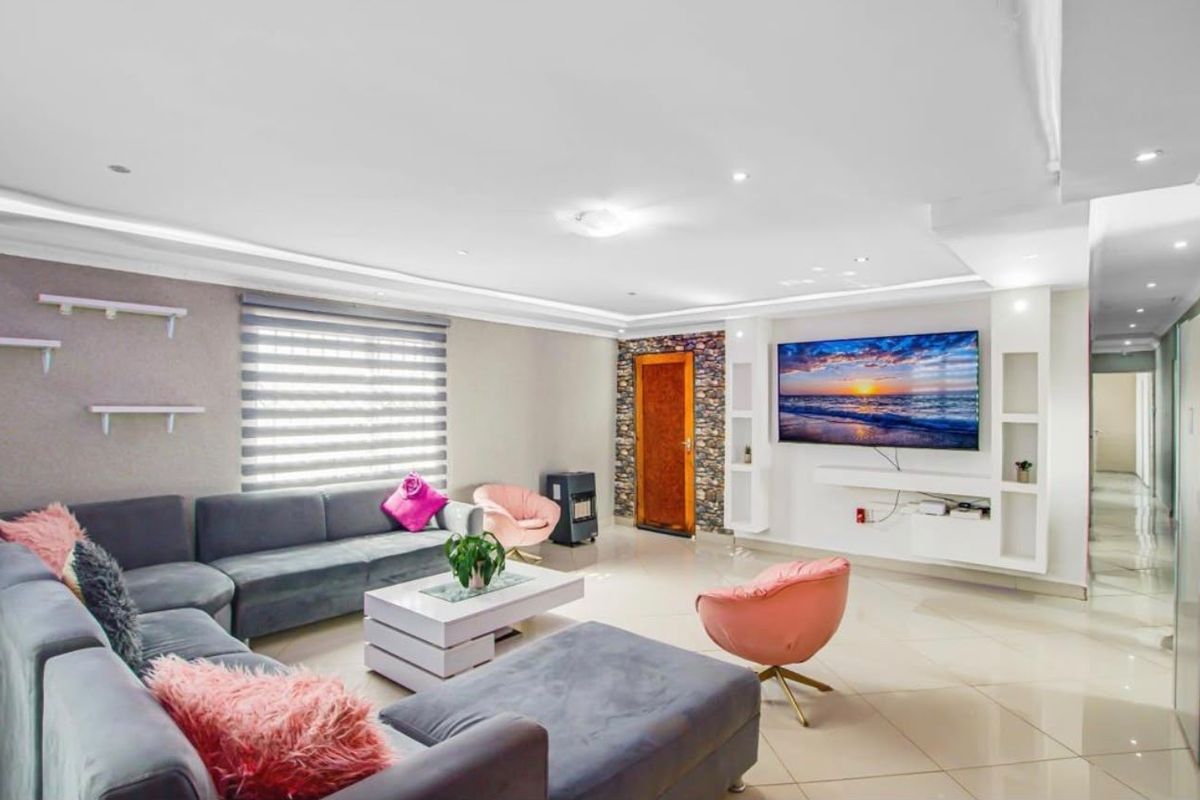 Spacious living room featuring tiled flooring, recessed ceiling lighting, a stone accent wall, and custom built-in shelving units.