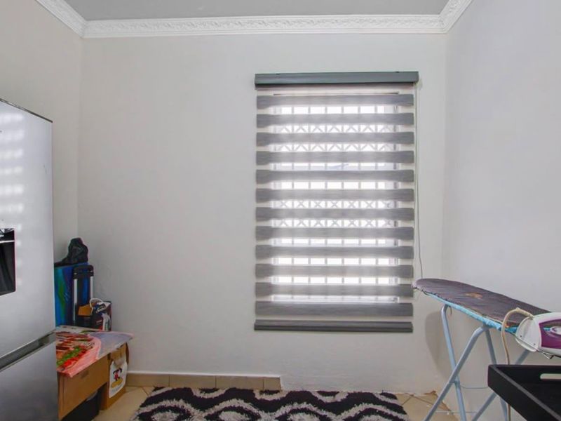 A functional laundry area featuring neutral walls, decorative ceiling cornicing, and a window fitted with modern roller blinds.
