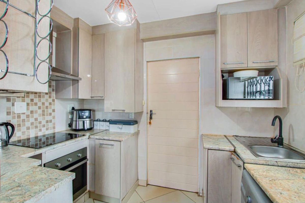 A functional kitchen featuring light wood cabinetry, granite countertops, a built-in oven with hob, and a tiled backsplash.
