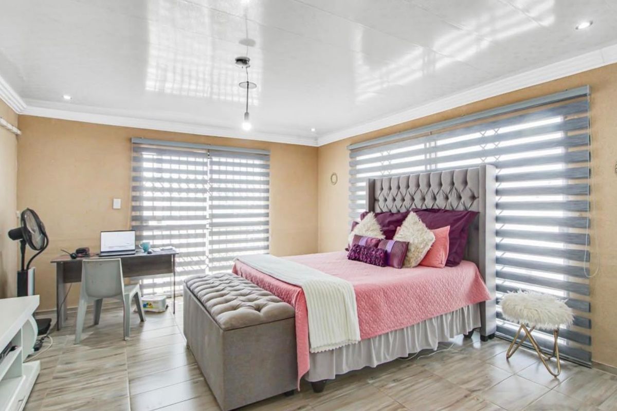A spacious bedroom featuring tiled flooring, recessed ceiling lighting, and large sliding glass doors with modern zebra blinds for adjustable natural light.