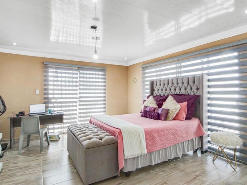A spacious bedroom featuring tiled flooring, recessed ceiling lighting, and large sliding glass doors with modern zebra blinds for adjustable natural light.