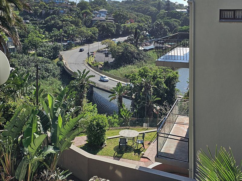 Elevated view overlooking a lush green landscape, a river, and a bridge, featuring a balcony and paved outdoor area.