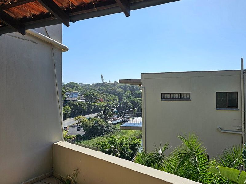 A balcony area featuring tiled flooring and a parapet wall, offering an elevated view of the surrounding neighborhood and greenery.