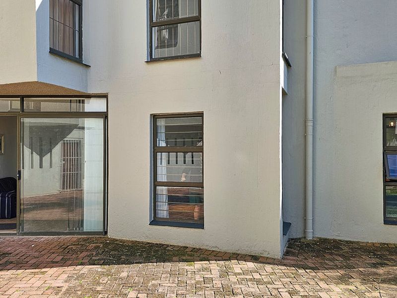 Rear exterior view of the apartment featuring brick paving, sliding glass doors, and casement windows with security bars.