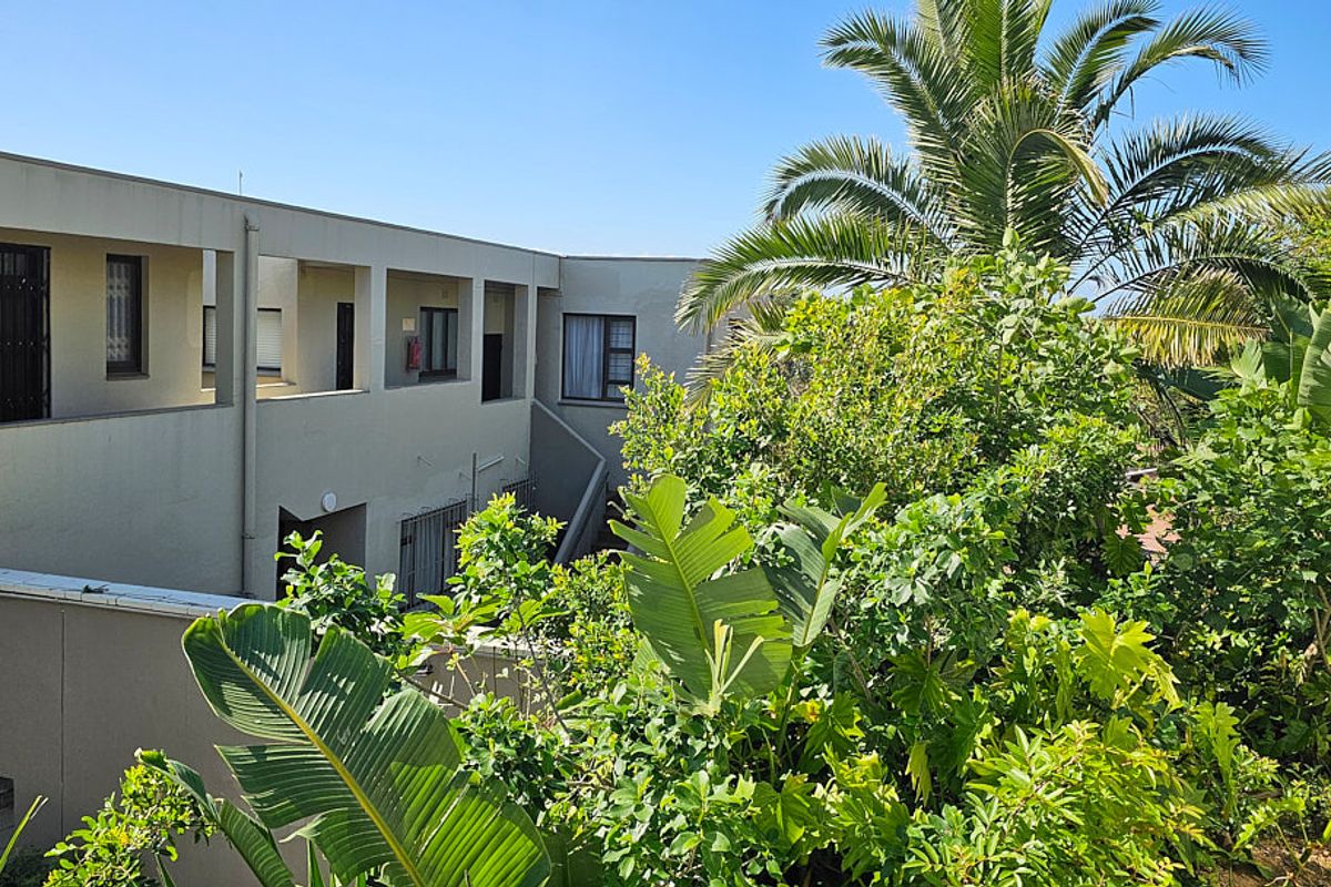 Rear view of the apartment building featuring a concrete facade, balcony walkways, and established garden landscaping.