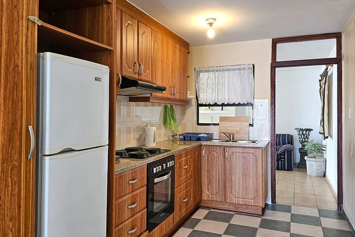 Functional kitchen featuring wooden cabinetry, built-in oven, hob, extractor fan, and double sink with tiled backsplash and flooring.