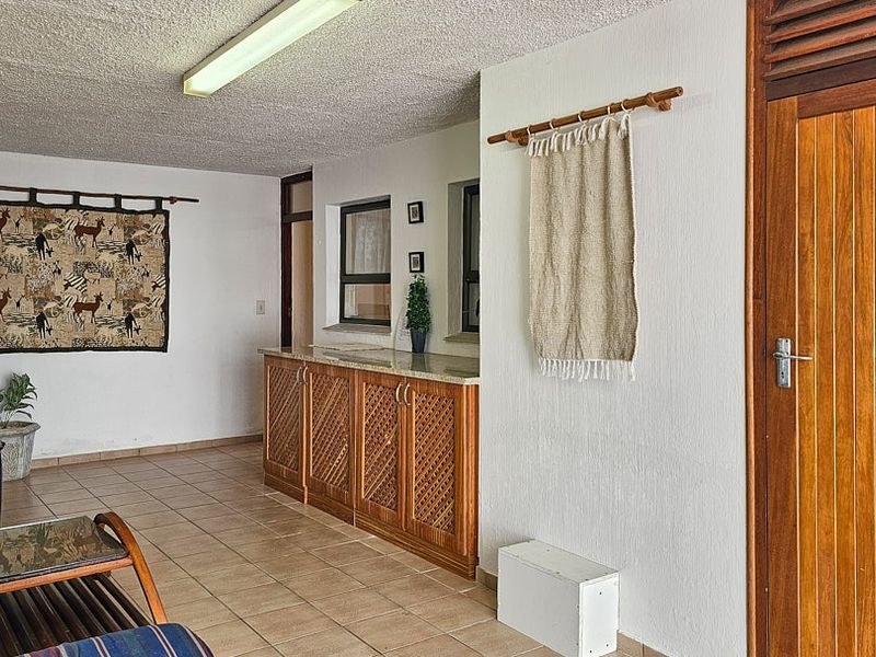 A covered patio area featuring tiled flooring, built-in cabinetry with stone countertops, and a solid timber door.