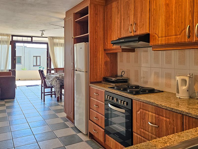 Open-plan kitchen and living area featuring wooden cabinetry, granite countertops, and tiled flooring, leading out to a balcony.